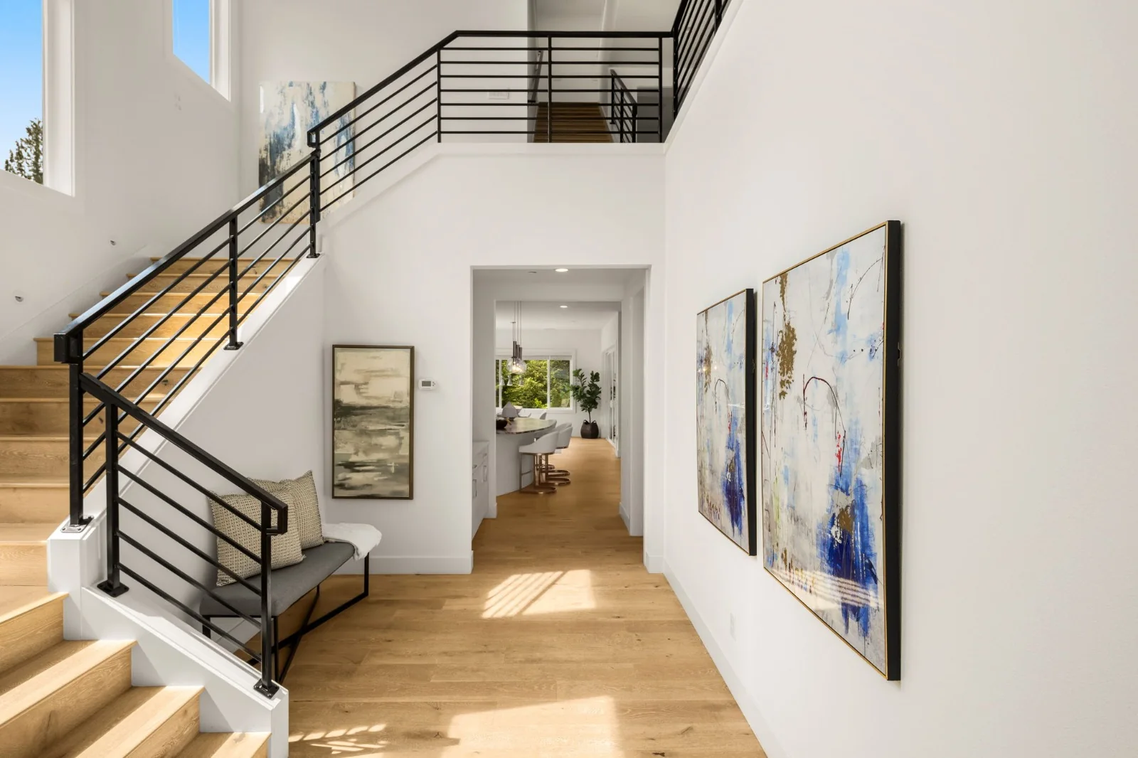 Light-filled entry with a black-railed staircase, wood floors, and colorful framed artwork