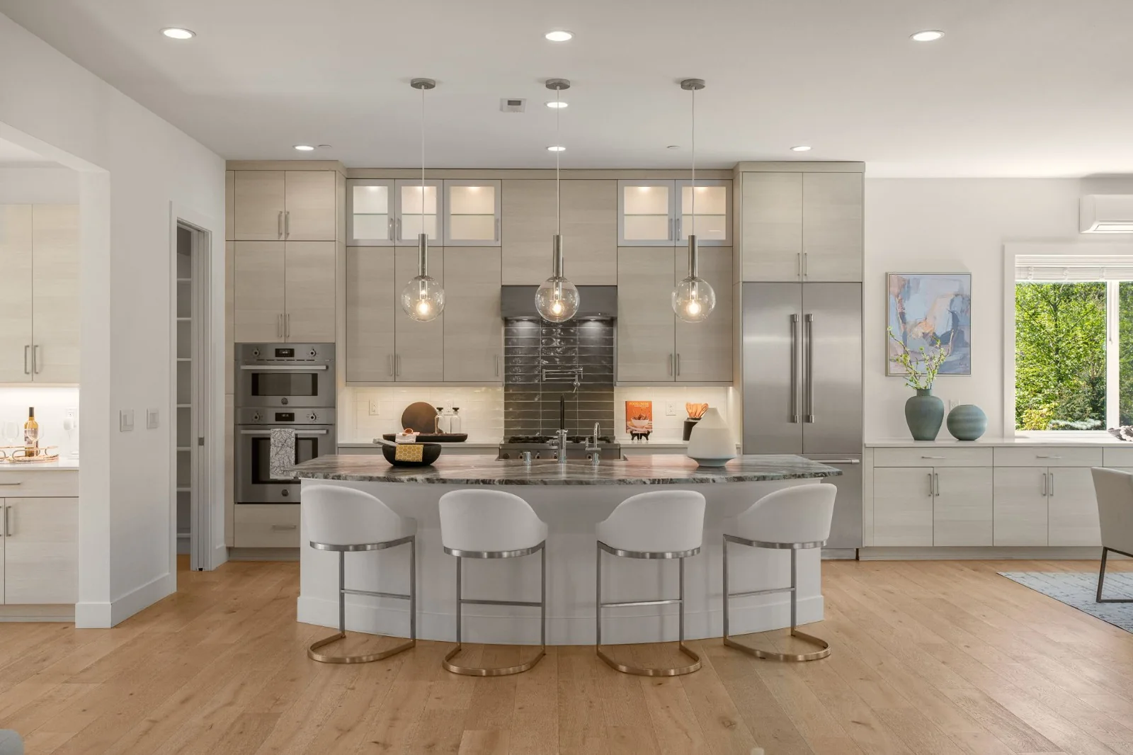Bright kitchen with a broad island, white stools, and pendant lighting
