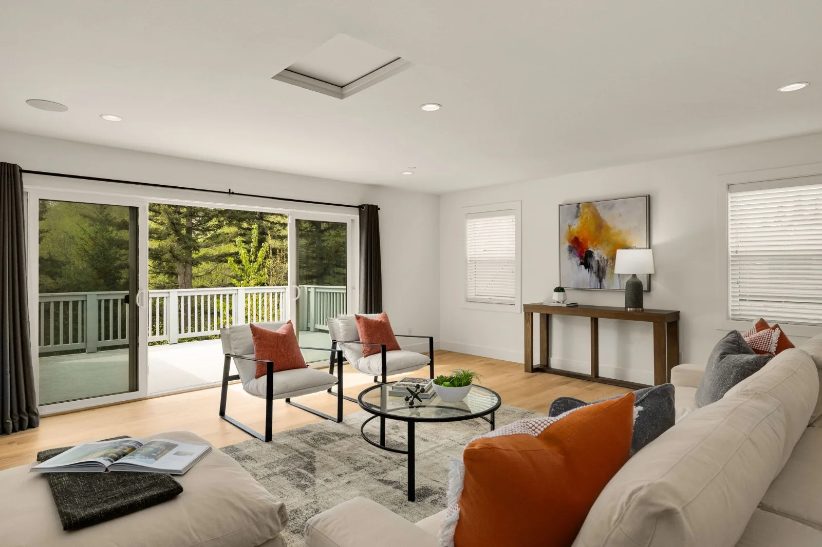 Living room with a cream sofa, rust-colored cushions, and open doors to a tree-lined terrace